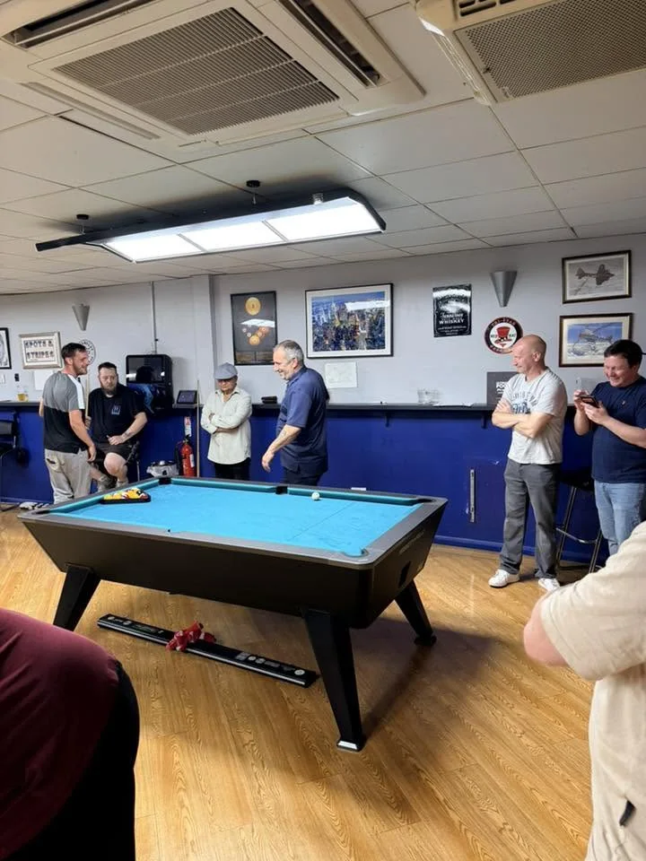 A pool table with blue cloth and players in the Spots & Stripes club room
